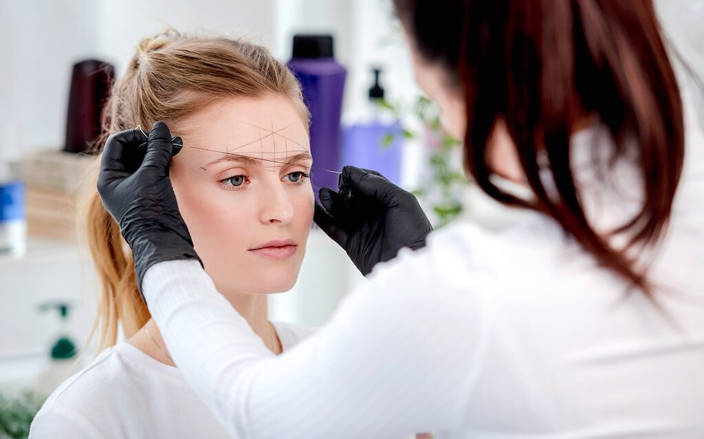 Woman receiving eyebrow mapping for microblading