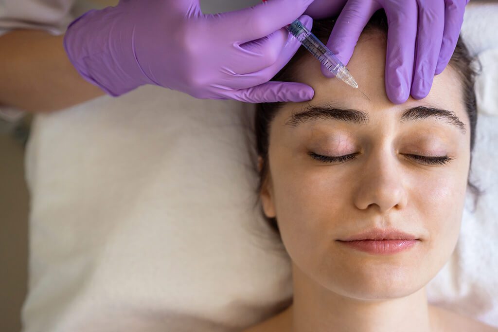 Relaxed woman with closed eyes receiving forehead injection